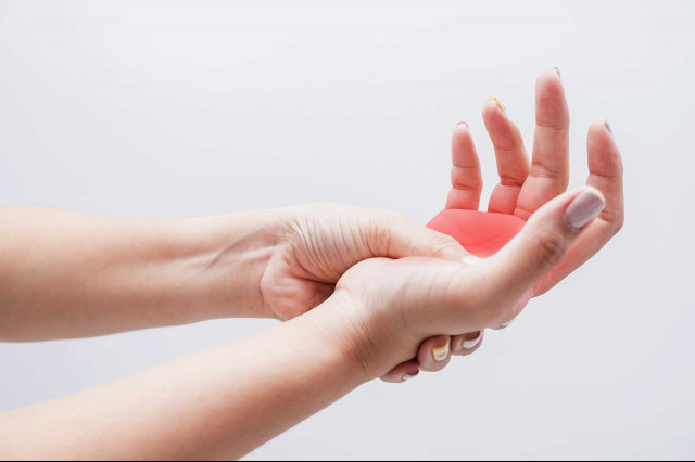 Degenerative rheumatische Erkrankungen - Eine weibliche Person hält ihre offene Hand und übt Druck auf die Innenseite aus.