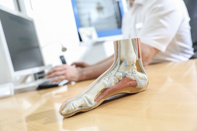 Fuchirurgie - Ein Mann sitzt an einem Schreibtisch mit Monitor und betrachtet ein Fumodell, das vor ihm auf dem Tisch liegt.